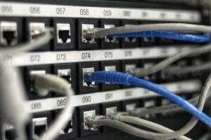 Close-up de cabos de rede conectados a portas numeradas em um patch panel, mostrando uma seção de hardware de rede em uso.
