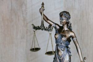 Estátua de bronze da Lady Justice segurando uma balança equilibrada na mão esquerda e uma espada na direita, usando uma venda nos olhos em um fundo neutro.