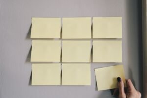 Nove notas adesivas amarelas estão dispostas em uma grade em uma parede, com uma mão removendo a nota inferior direita.