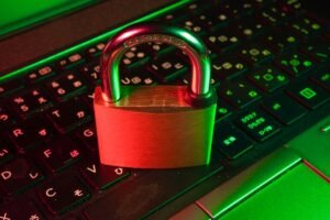 Um cadeado de latão fica em um teclado de laptop preto com iluminação vermelha e verde, simbolizando a segurança cibernética ou a proteção de dados.