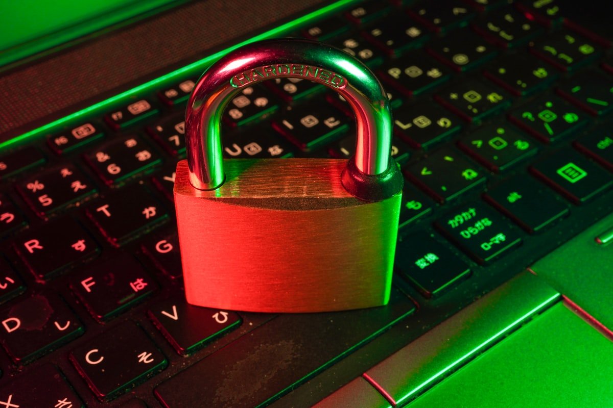 Um cadeado de latão fica em um teclado de laptop preto com iluminação vermelha e verde, simbolizando a segurança cibernética ou a proteção de dados.