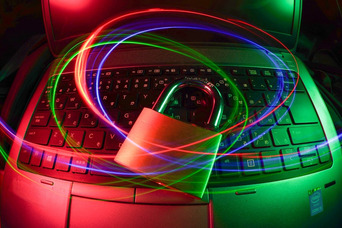 Um cadeado fica em um teclado de laptop com trilhas de luz coloridas girando acima, simbolizando a segurança cibernética ou a proteção de dados.