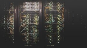 Fileiras de servidores de rede com cabos visíveis e luzes indicadoras estão alojadas em um rack escuro de data center.